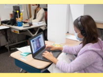 Female student working on laptop at desk with mask on